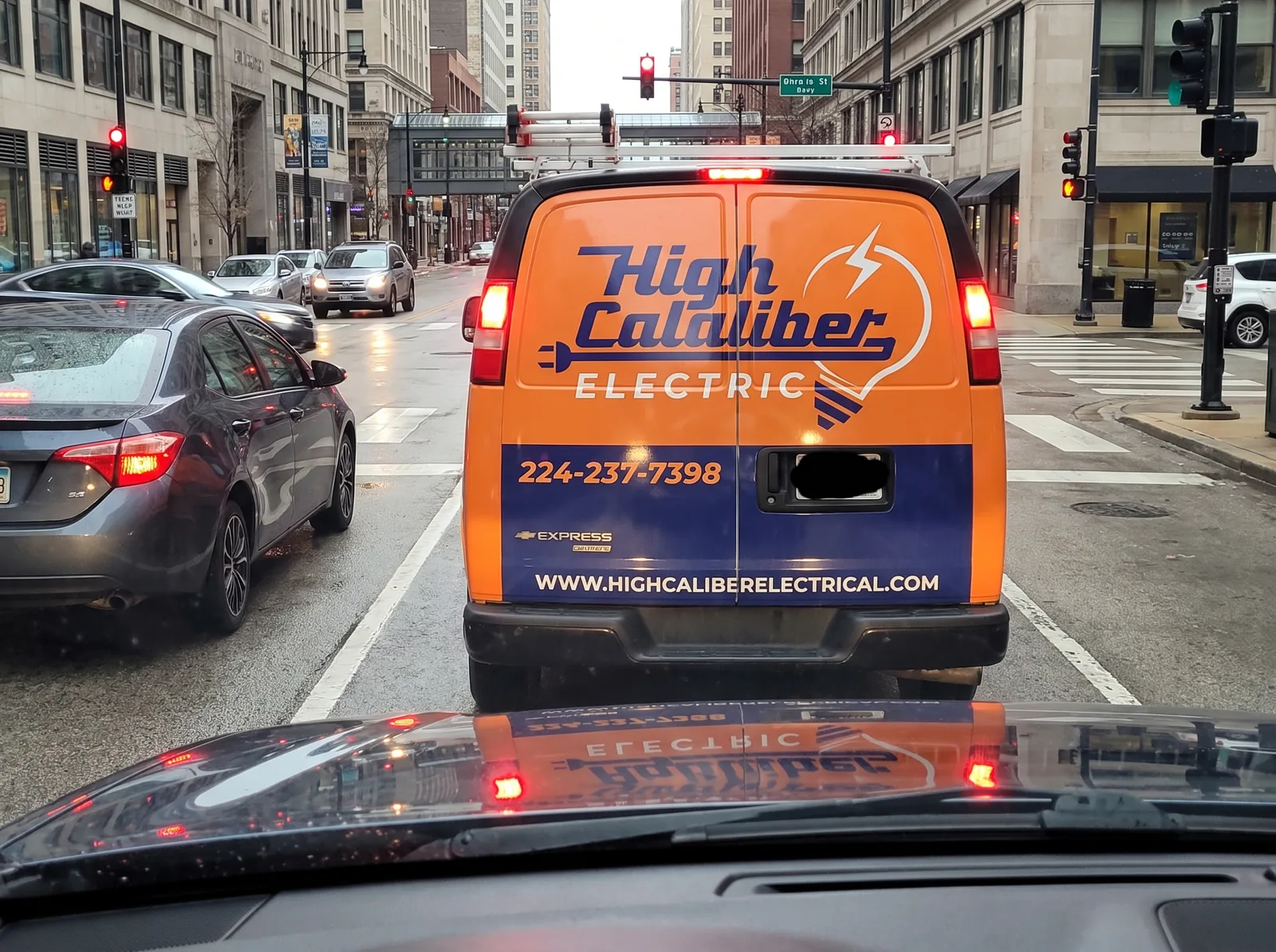 High Caliber Electric Chevy Express rear at a red light. Phone 224-237-7398 readable from the next car.