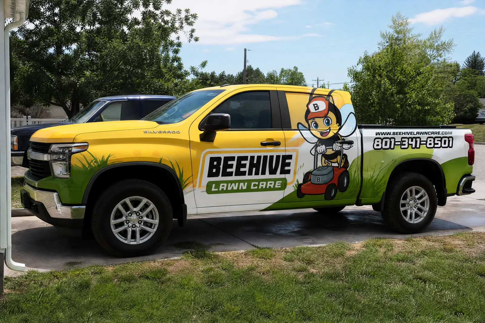 Beehive Lawn Care Silverado in a residential driveway, bee mascot, 801-341-8501 and beehivelawncare.com readable on the bed.